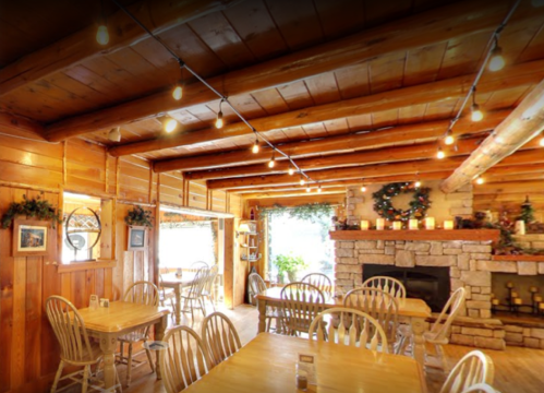 Cozy wooden restaurant interior with string lights, a stone fireplace, and rustic tables.