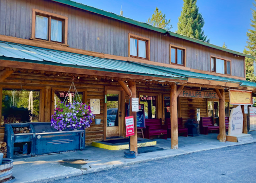 A rustic wooden lodge with a green metal roof, featuring a bar sign and flower baskets outside.