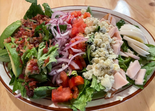 A colorful salad with lettuce, tomatoes, red onions, avocado, bacon, turkey, and blue cheese on a plate.