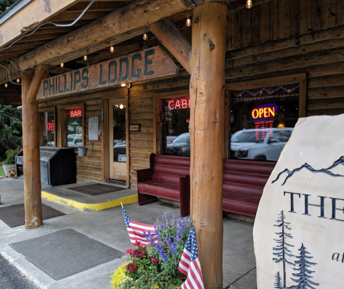 Exterior of Phillips Lodge featuring a wooden entrance, open sign, and flower beds with American flags.