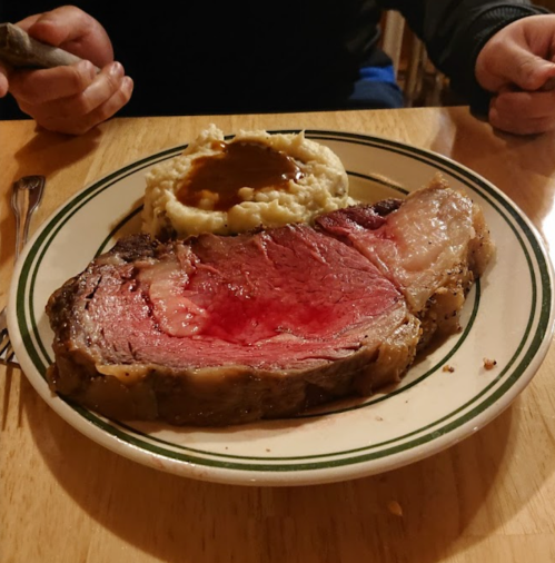 A plate with a large slice of prime rib, served with mashed potatoes and gravy, on a wooden table.