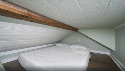 Cozy attic bedroom with a low ceiling, featuring a simple bed against a slanted wall and light green paint.