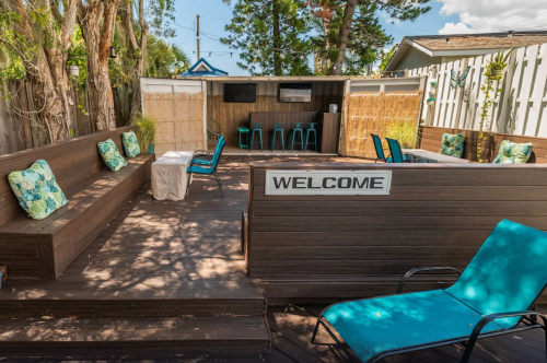 Outdoor seating area with blue chairs, a welcome sign, and a cozy atmosphere surrounded by greenery.