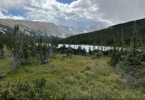 A scenic view of a mountainous landscape with a lake, surrounded by lush greenery and cloudy skies.