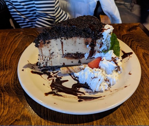 A slice of chocolate cake topped with whipped cream, chocolate drizzle, and a strawberry, served on a white plate.