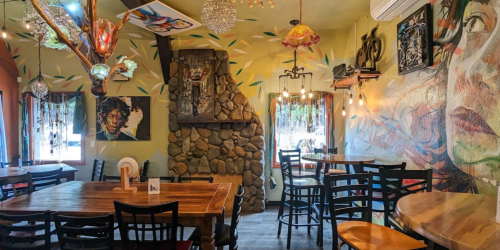 Cozy restaurant interior featuring colorful murals, a stone fireplace, and wooden tables with black chairs.