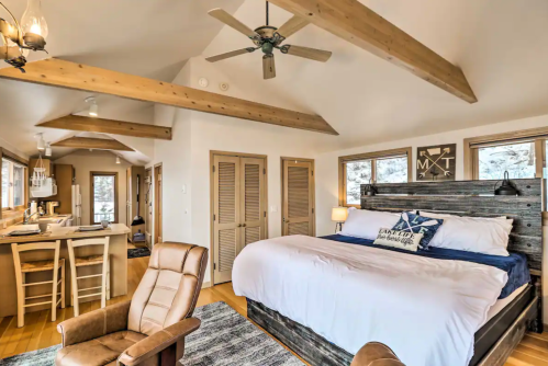 Cozy bedroom with wooden beams, a large bed, and a seating area, featuring natural light and a rustic decor style.