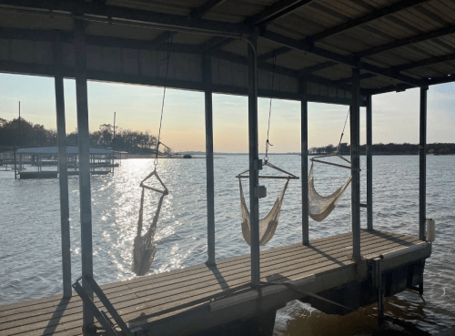 Hammocks hanging on a dock overlooking a calm lake at sunset, with gentle ripples on the water's surface.