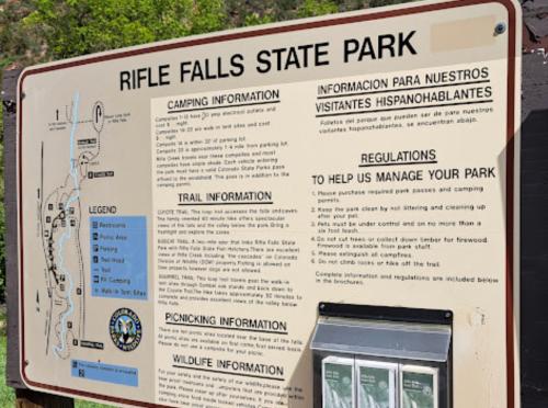 Signboard at Rifle Falls State Park detailing camping, trail, picnicking, and wildlife information in English and Spanish.