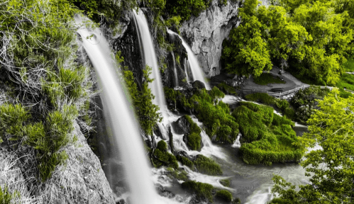 A serene waterfall cascading over rocks, surrounded by lush greenery and a peaceful landscape.
