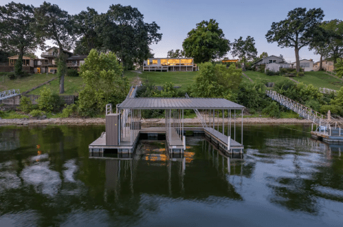 A serene lakeside scene featuring a dock, calm water, and houses on a hillside at dusk.