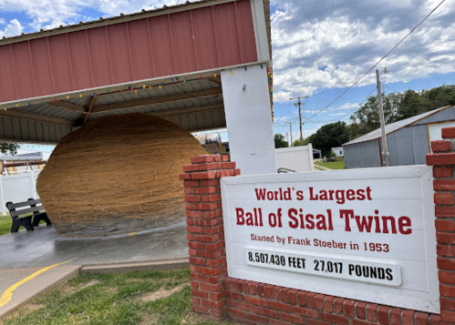 A large ball of sisal twine displayed under a shelter, with a sign detailing its size and weight.