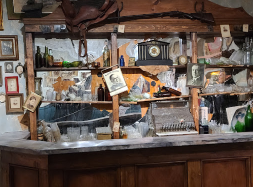 A vintage bar display with old photographs, bottles, and a cash register, set against a rustic wooden backdrop.