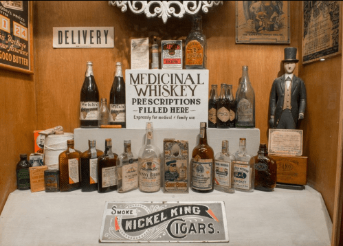 A display of vintage bottles, a sign for medicinal whiskey prescriptions, and a cigar advertisement in a rustic setting.
