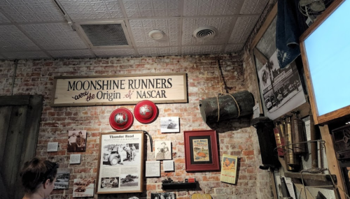 A rustic wall display featuring a sign about moonshine runners and NASCAR, with historical photos and artifacts.
