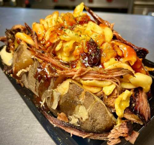 A loaded baked potato topped with pulled pork, macaroni, and barbecue sauce, served on a black tray.