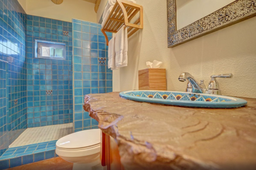 A modern bathroom featuring a blue tiled shower, stone sink, and wooden accents.