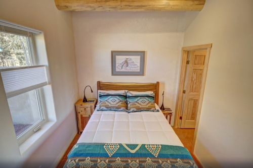 Cozy bedroom featuring a wooden bed, colorful bedding, a bedside table, and a window with natural light.