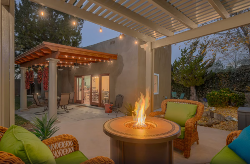 Cozy outdoor patio with a fire pit, seating, and string lights, surrounded by trees and a warm evening ambiance.