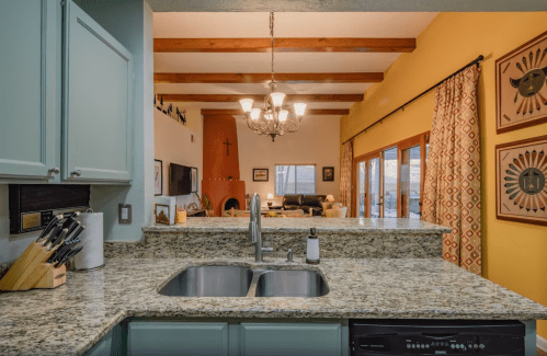A modern kitchen with granite countertops, a sink, and a view of a cozy living room with warm decor and large windows.