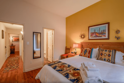 Cozy bedroom with colorful decor, a large bed, and a hallway leading to a bathroom and another room.