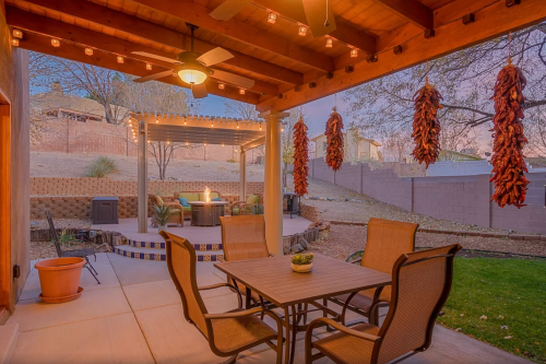 Cozy outdoor patio with a table, chairs, and a fire pit, surrounded by string lights and hanging decorations.