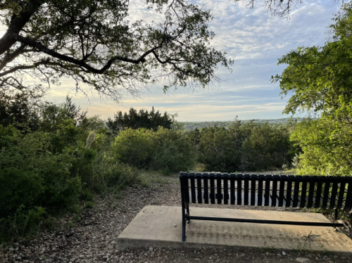 A bench overlooks a scenic view of greenery and a cloudy sky, inviting relaxation in nature.