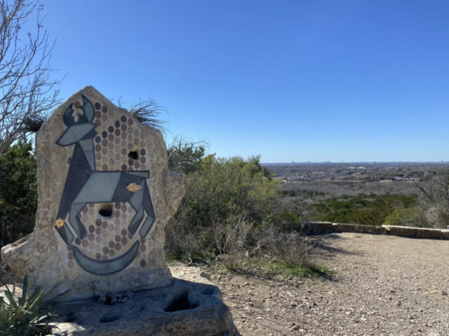 A decorative stone sculpture of a deer overlooks a scenic view of a city skyline and clear blue sky.