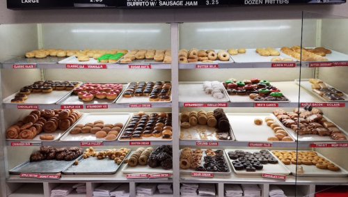 A display case filled with various donuts, including glazed, chocolate, and filled options, alongside fritters.