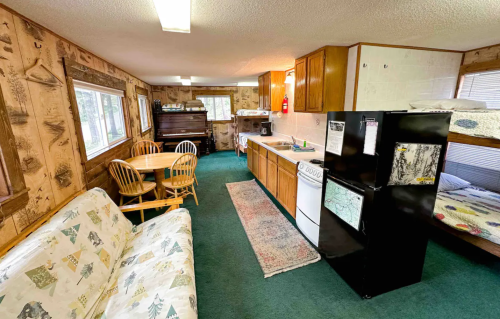 Cozy cabin interior featuring a kitchen, dining area, and bunk beds, with wood-paneled walls and green carpet.