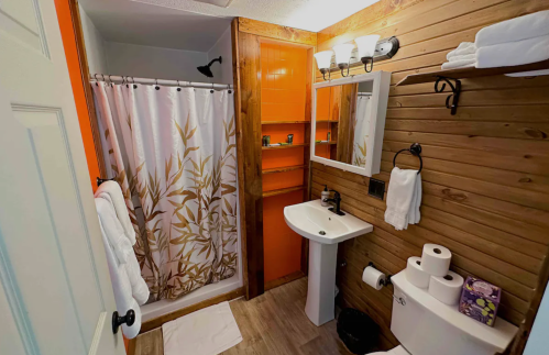 Cozy bathroom featuring a shower, sink, wooden accents, and neatly arranged towels and toiletries.