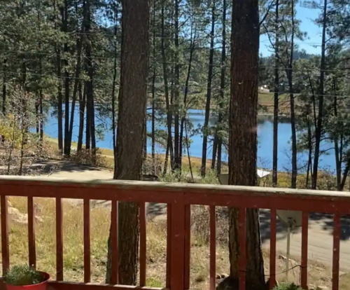 A scenic view of a lake surrounded by trees, seen from a wooden deck on a sunny day.