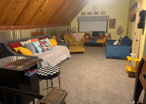 Cozy attic living room with colorful furniture, a retro arcade game, and wooden beams on the ceiling.