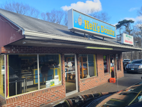 Exterior of Neil's Donuts shop with a blue sign, brick facade, and large windows on a sunny day.