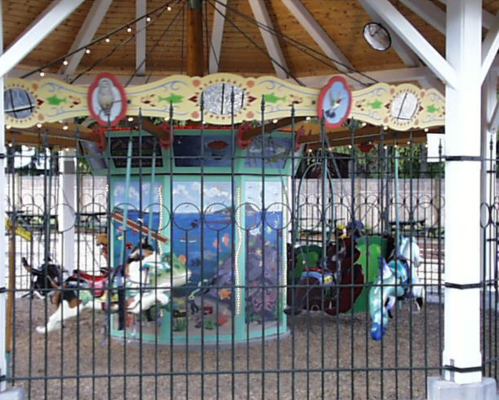 A colorful carousel with various animals, surrounded by a decorative fence and a wooden structure overhead.