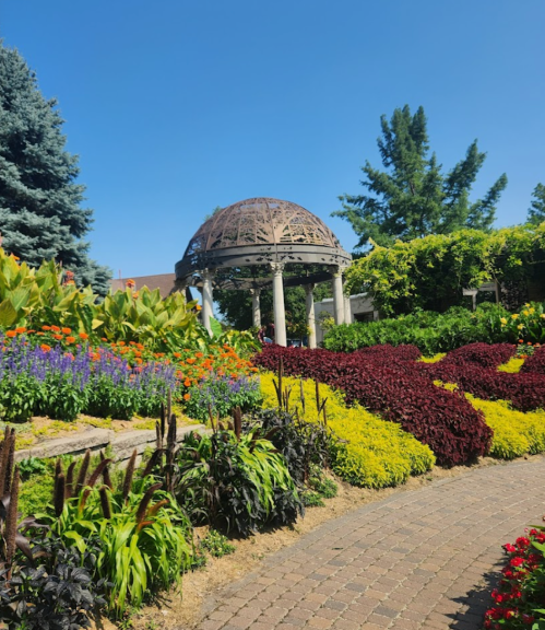 A vibrant garden with colorful flowers, a stone pathway, and a decorative gazebo under a clear blue sky.