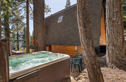 A hot tub surrounded by trees, with a wooden cabin in the background and a clear sky above.