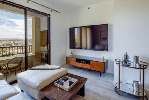 Modern living room with a large TV, stylish furniture, and a view of the outdoors through sliding glass doors.