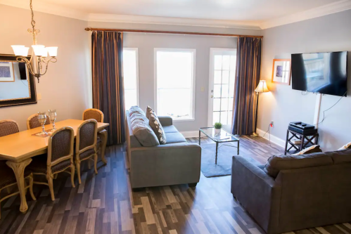 Cozy living and dining area with a table, chairs, sofas, and large windows letting in natural light.