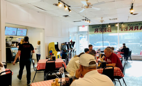 A casual diner with checkered tablecloths, arcade games, and patrons enjoying their meals. Bright and inviting atmosphere.