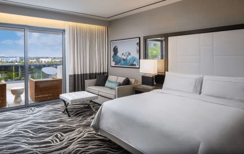 Modern hotel room featuring a king bed, seating area, and balcony with a view. Stylish decor and natural light.