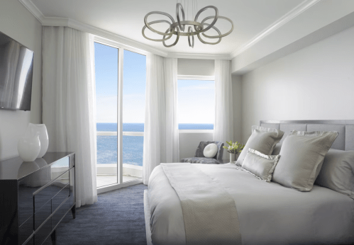Modern bedroom with ocean view, large windows, light curtains, and stylish decor.