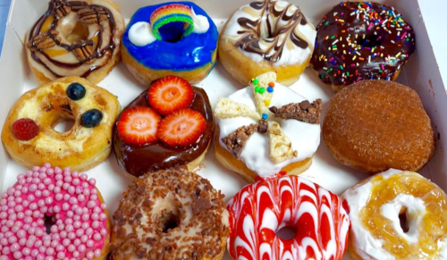 A box of assorted donuts featuring various toppings like sprinkles, fruit, and chocolate.