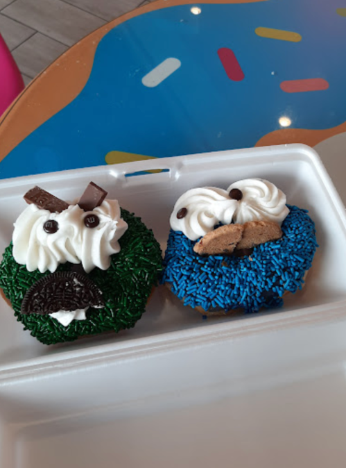 Two decorated donuts: one with green sprinkles and a cookie monster design, the other with blue sprinkles and a monster face.