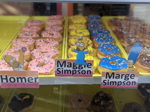 A display of colorful donuts with cartoon character cutouts of Homer, Maggie, and Marge Simpson.
