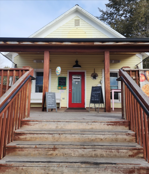 A yellow house with a red door and wooden steps, featuring chalkboards and decorations at the entrance.