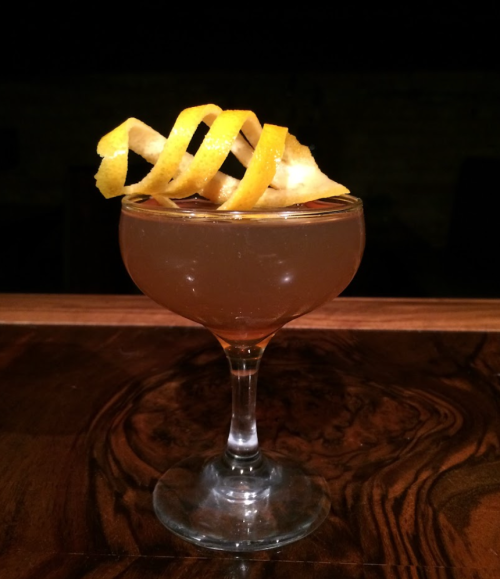 A cocktail in a stemmed glass, topped with spiral lemon peels, resting on a wooden surface.