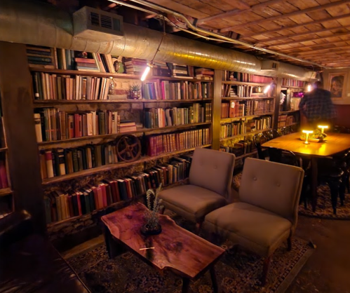 Cozy basement library with bookshelves, a wooden table, and comfortable seating under warm lighting.