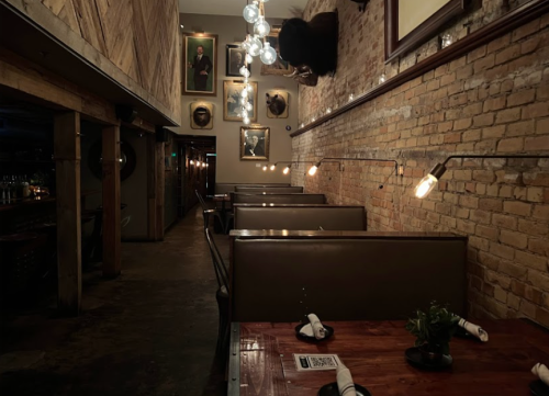 Cozy restaurant interior with wooden tables, leather booths, and vintage portraits on exposed brick walls.
