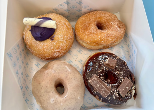 A box of four assorted donuts: one with purple frosting, a sugar-coated donut, a cinnamon donut, and a chocolate-topped donut.